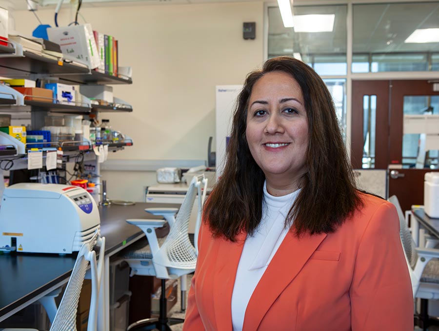Woman in a coral-colored blazer stands in a laboratory setting.