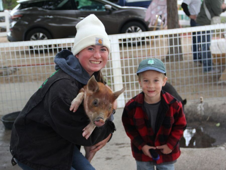 A smiling woman holding a piglet standing beside a smiling boy.