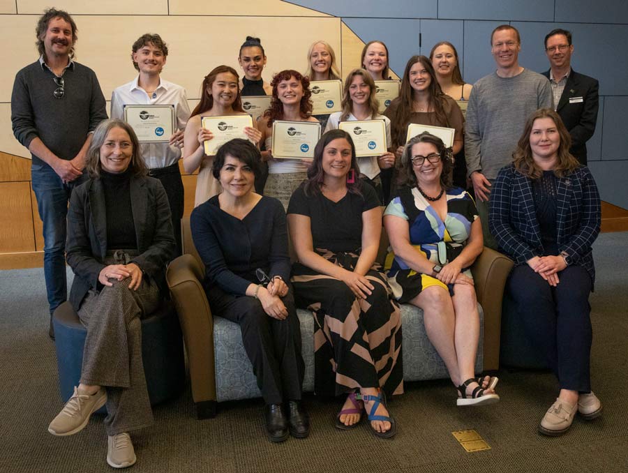 A group of people, some sitting and some standing, smile for a photo with students holding up certificates.
