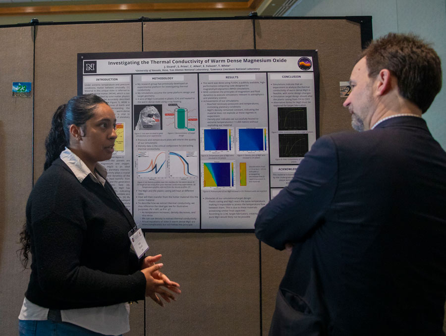 A woman and man speak in front of a scientific poster.