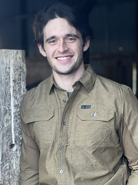 Joe Hill wearing a brown button-up shirt, standing in a barn.