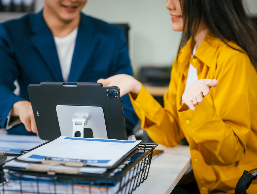 A businessman and businesswoman are working together at a desk, using a laptop. They are discussing business strategies, financial planning, and collaboration.