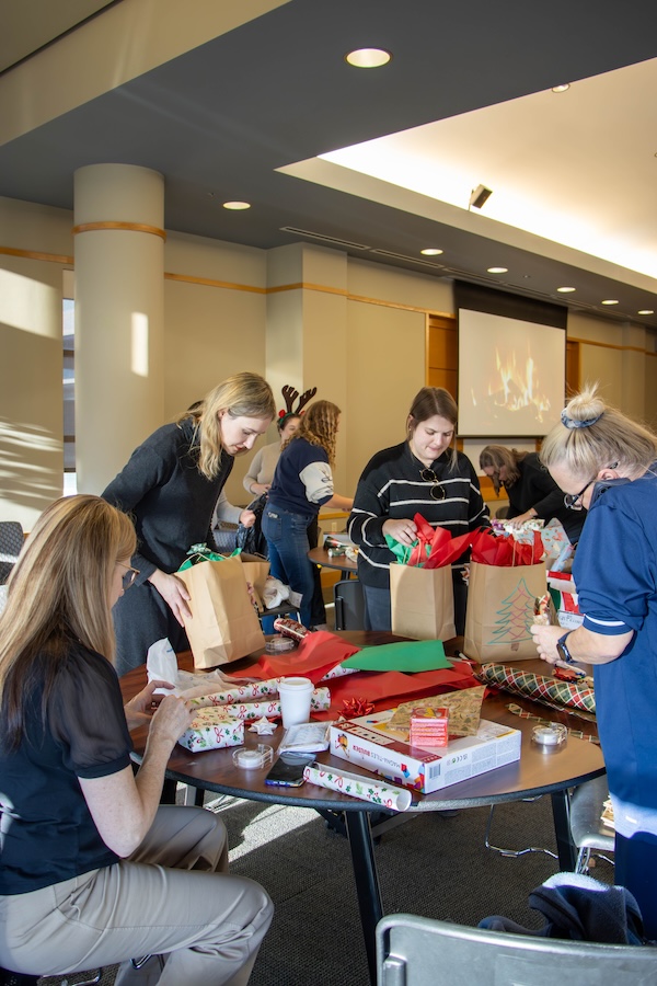 A group of faculty members chatting and wrapping presents.