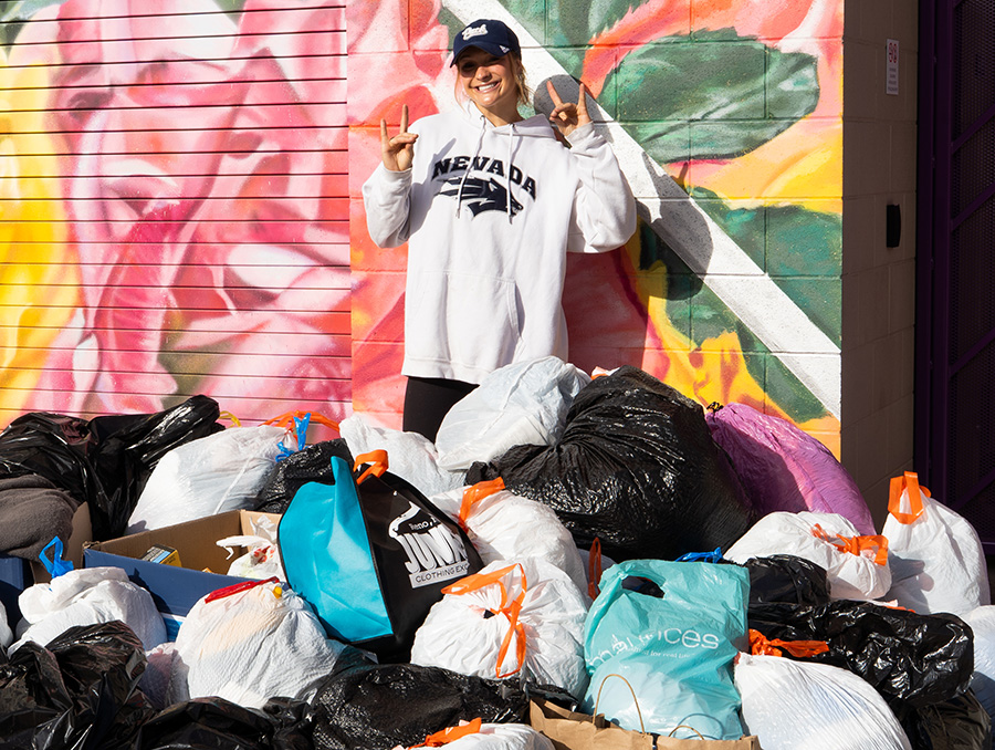 Karolyn Glover gives the Wolf Pack hand signs while standing among bags of donated items.
