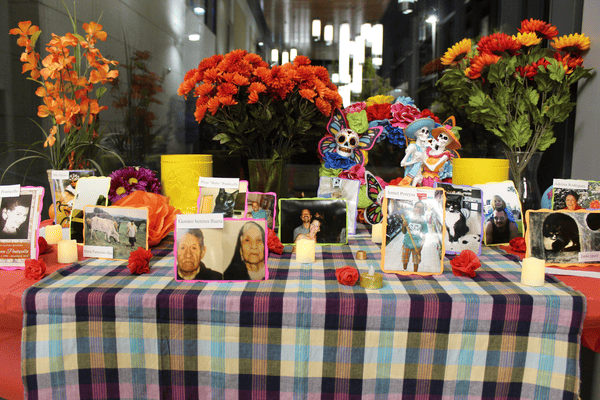 An altar at the Beyond Borders event with photos of people and pets, marigold flowers, and candles.