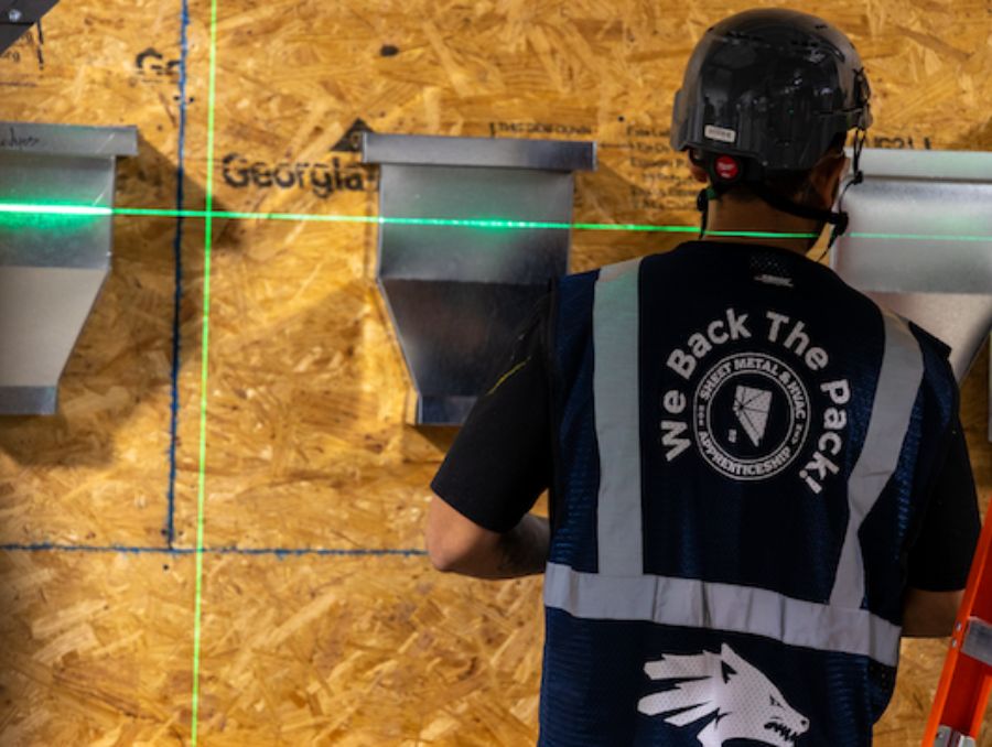 A construction apprentice installing vents on a wall.