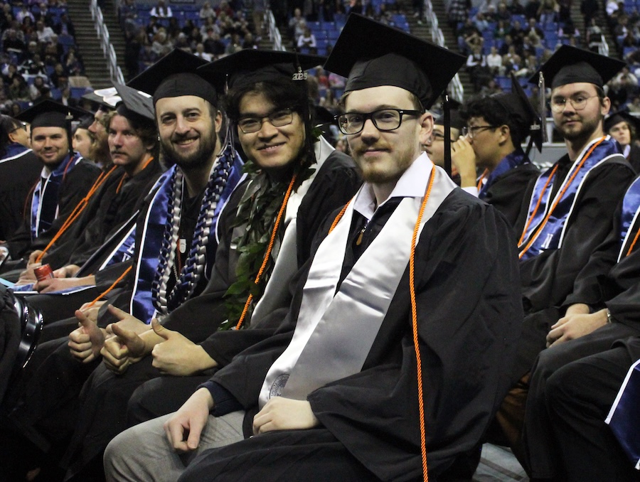 Graduates sitting while dressed in cap and gowns during commencement.