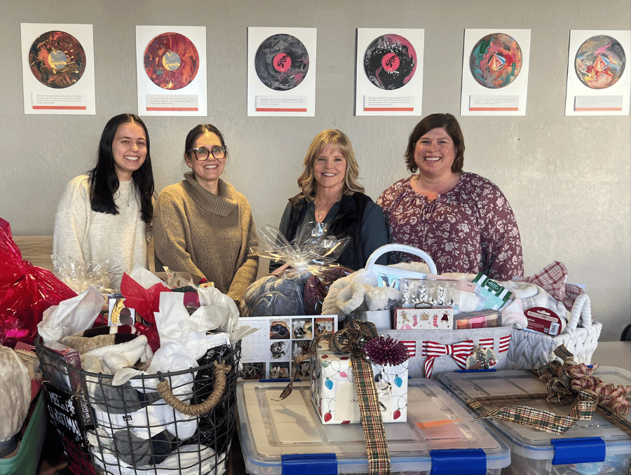 Four employees of the Sanford Center for Aging are standing behind wrapped gifts donated by Grace Church Widows Group.