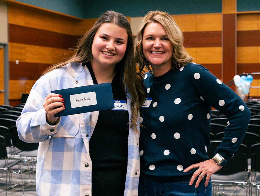 Sarah Leary (left) holds an envelope with her student teaching assignment.. Jamie Gustafson (right) stands next to Sarah and smiles. 