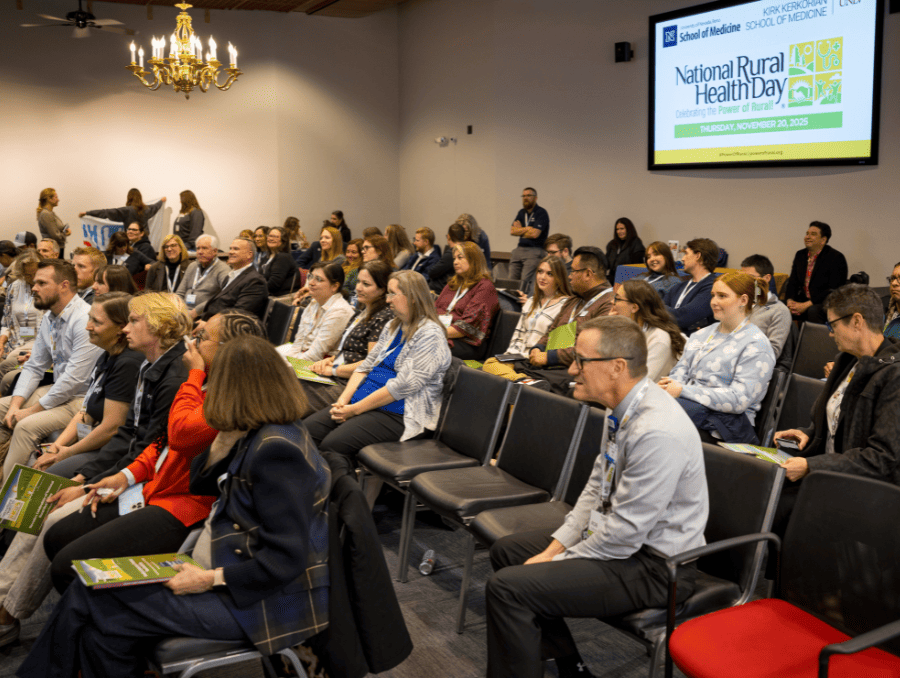 A group of people looking at a speaker in a lecture setting with National Rural Health Day on a screen behind them.