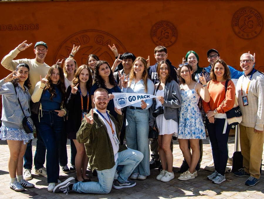 Faculty and students in Paris for the French Open with one student holding a University pennant flag. 