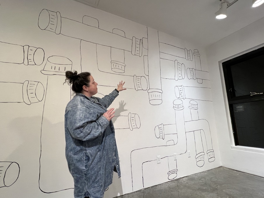 Artist points to her work in gallery. 