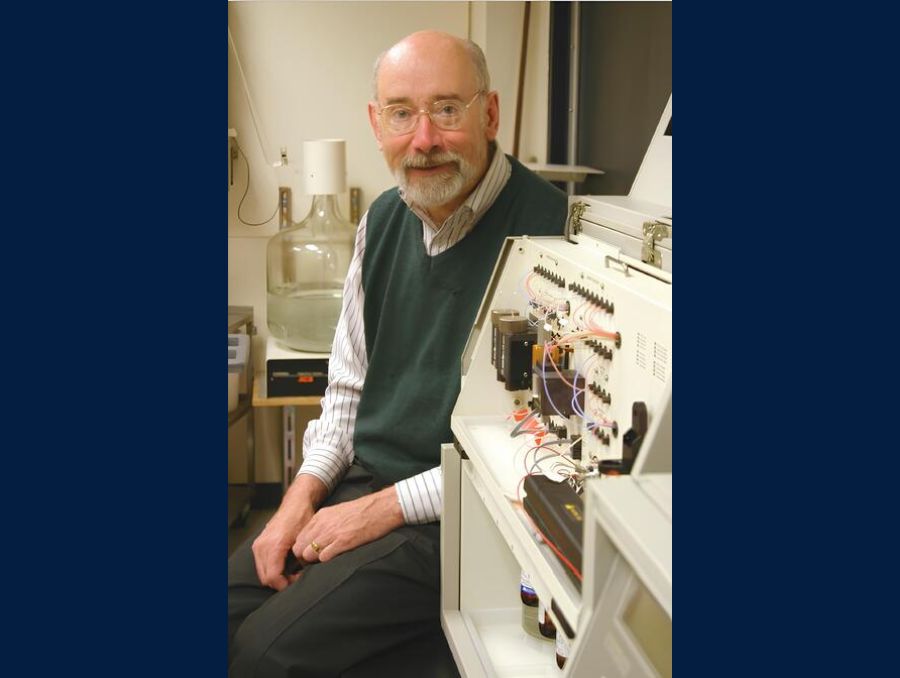 A man in glasses sitting by a wired ab equipment. 