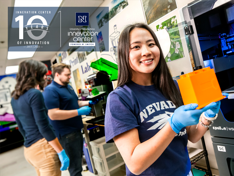 Person holding an orange object in a laboratory at the UNR Innevation Center, with two other individuals working in the background.