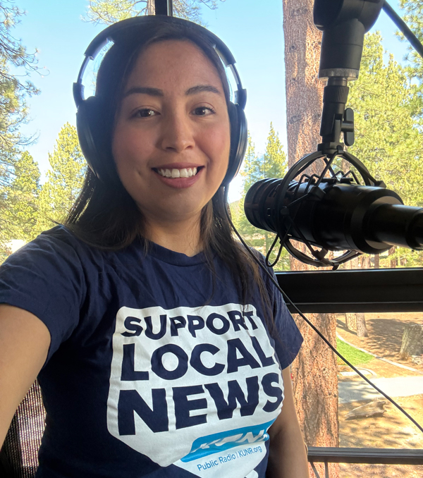 Maria Palma behind the mic in the KUNR Lake Tahoe studio wearing headphones and a shirt that says "Support local news."