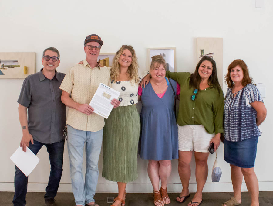 A group of Allen's colleagues posing for a picture in  front of her artwork.