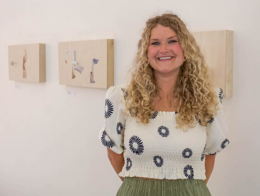 Molly Allen stands in front of her artwork in a gallery.