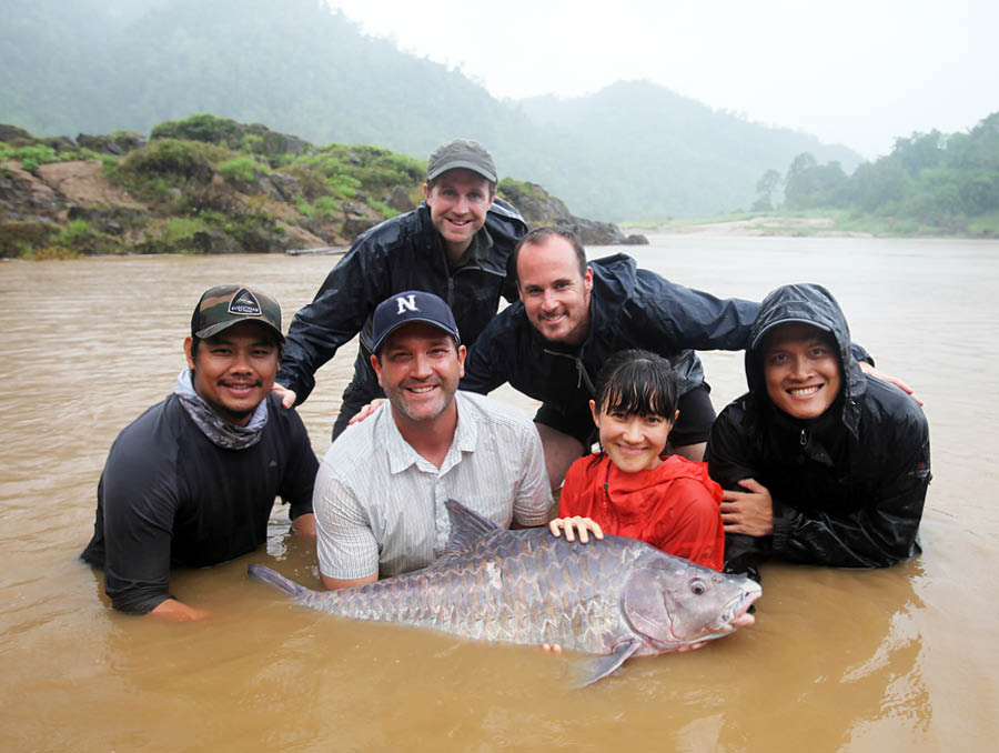 Dr. Zeb Hogan and his team standing in the middle of a river holding a fish.