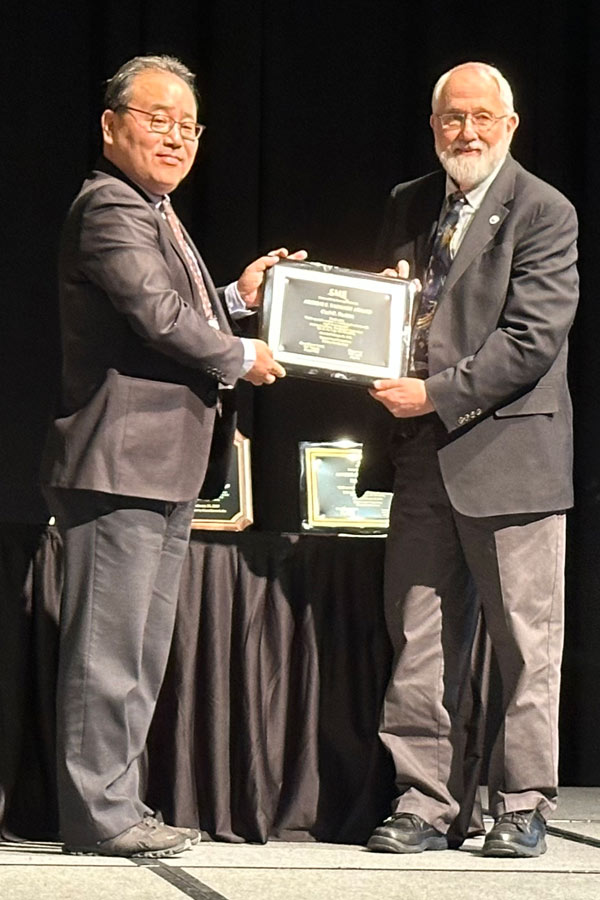 Two men stand on a stage, holding a plaque between them.