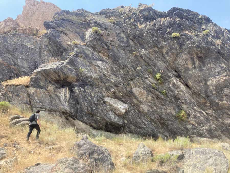 A man walking toward a rocky outcropping on a hillside.