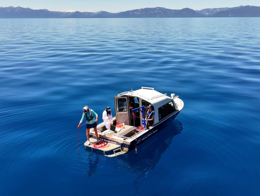 An aerial photo of a boat floating in Lake Tahoe with two people on it, taking research samples with equipment.