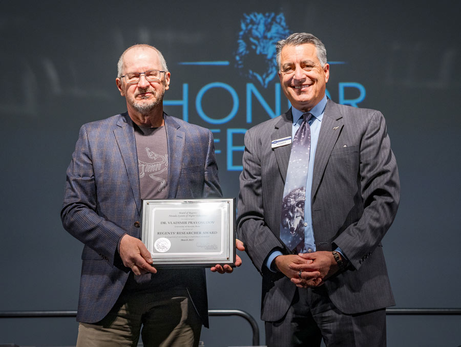Vladimir Pravosudov stands next to President Sandoval holding a certificate on a stage.