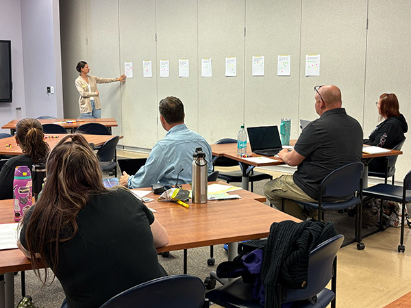 Person standing at the front of a conference room teaching a lesson to a group of people.