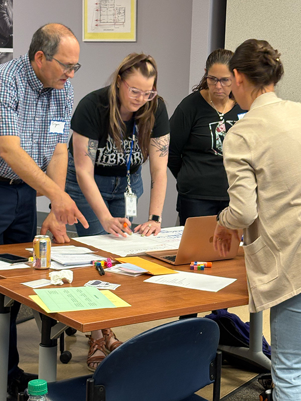 Four people standing around a table writing on papers and talking.