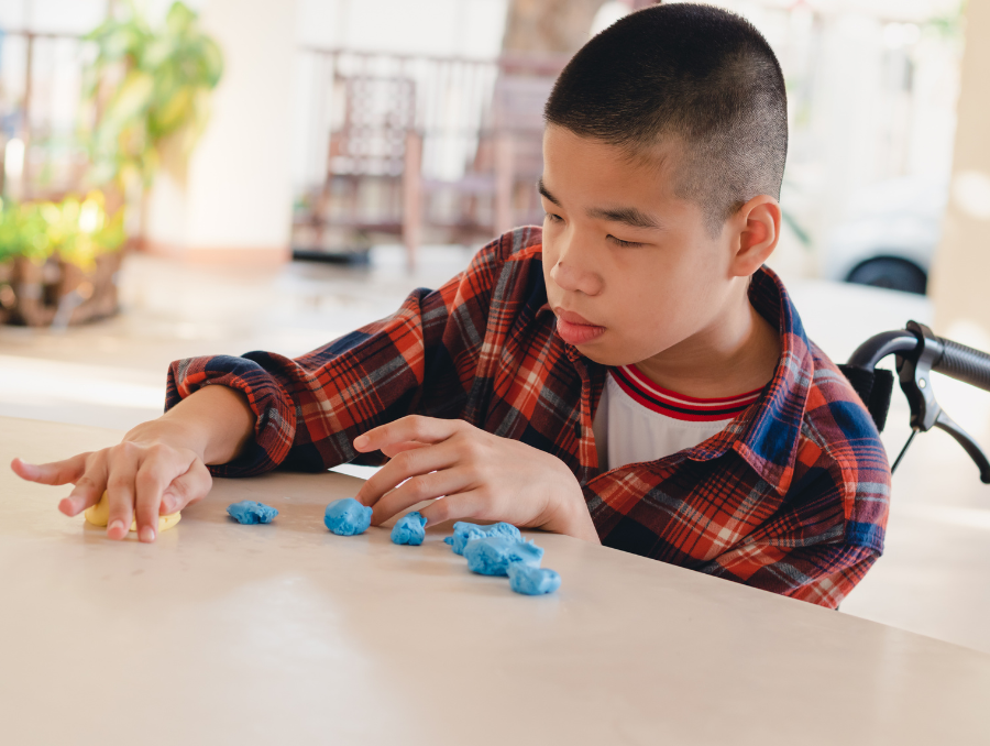 Child using a wheelchair and playing with blue and yellow squishable materials.