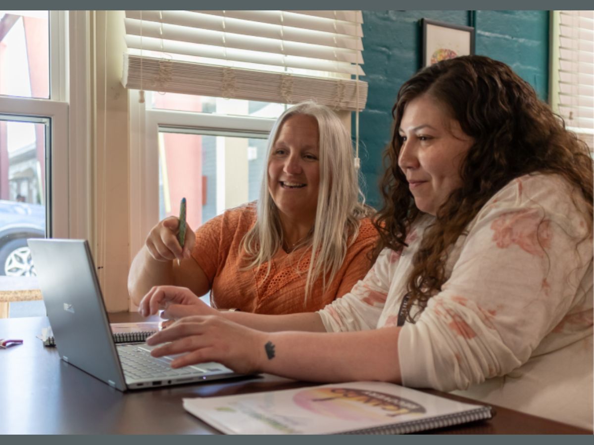Two women look at a computer together, smiling.