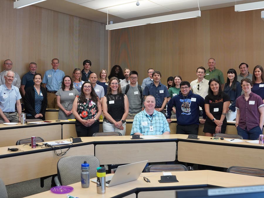 A group of people stand behind tiered desks in a classroom and smile for a photo.
