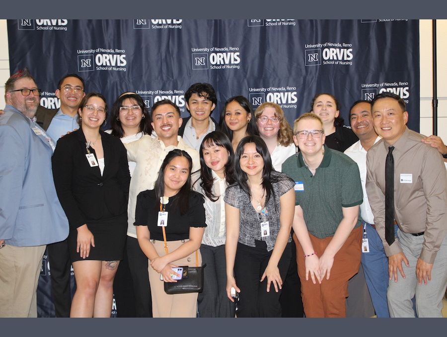 A large group of attendees pose together, smiling, in front of an Orvis School of Nursing step and repeat background.
