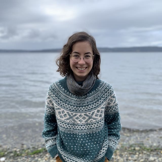 A smiling woman poses in front of a lake under gray clouds.