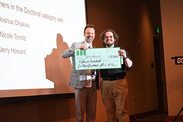 A man standing on stage, smiling while holding a giant check.