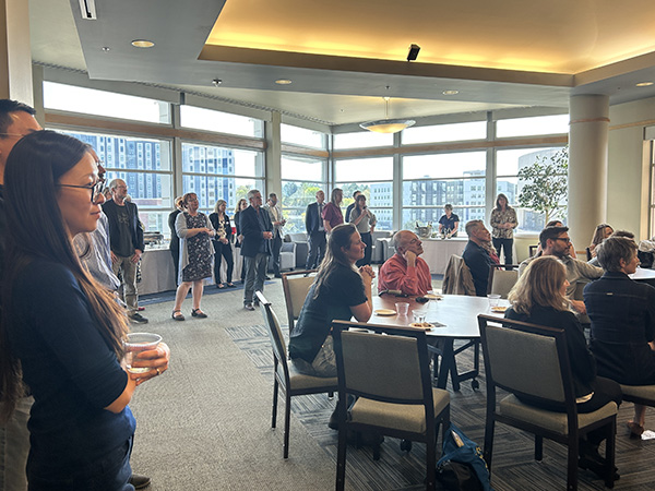 People attending a research awards ceremony at the Joe Crowley Student Union. with large windows offering a view of urban buildings.