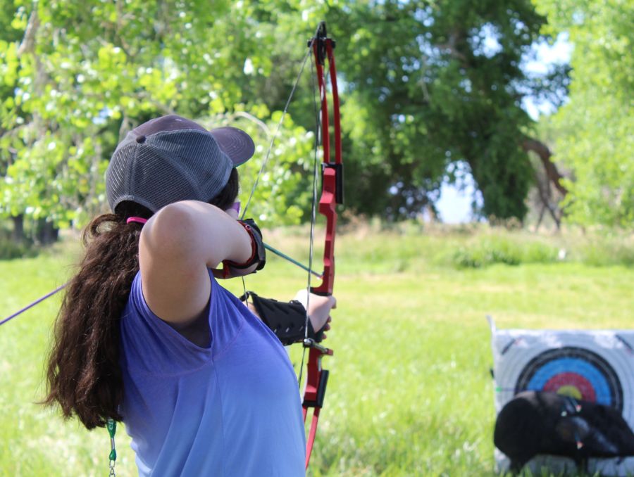A girl aims an arrow drawn from a bow towards a board with circular rings. 