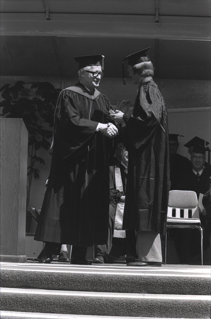 A student receives their degree and a handshake from a faculty member at commencement.
