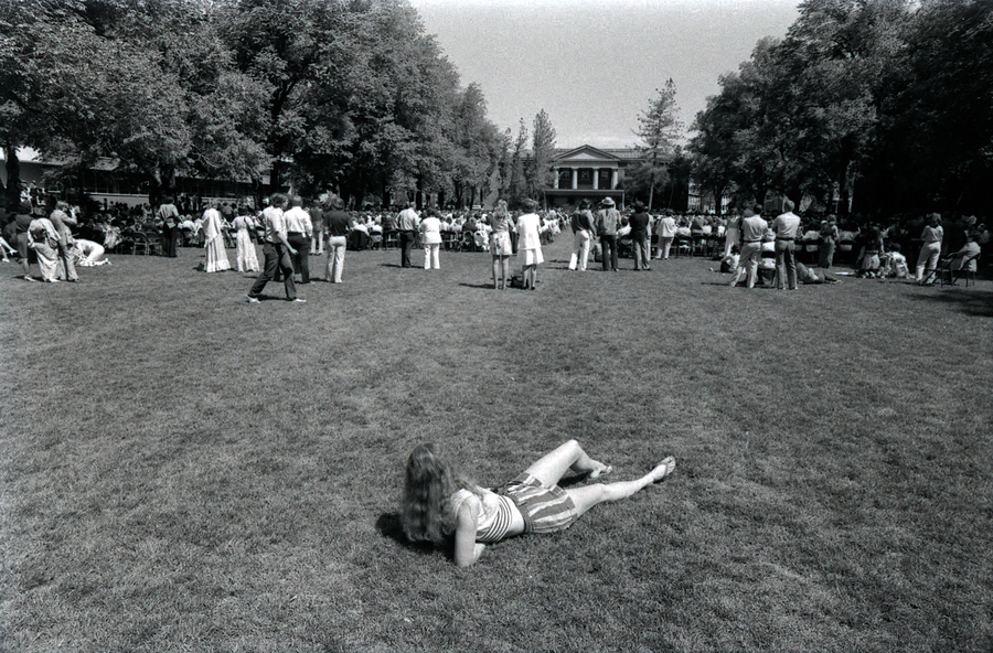 A woman lies on the grass of the Quad during commencement.