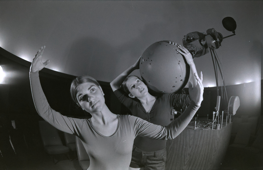 Two modern dancers pose inside the planetarium. One holds a large circular object.