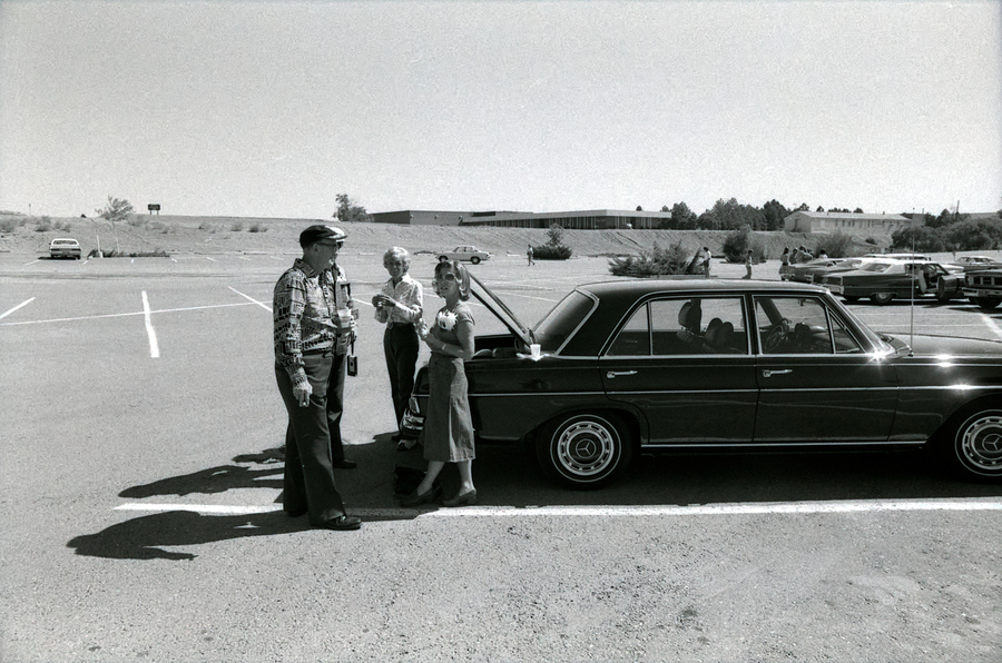 Four people stand by a car in an empty parking lot.