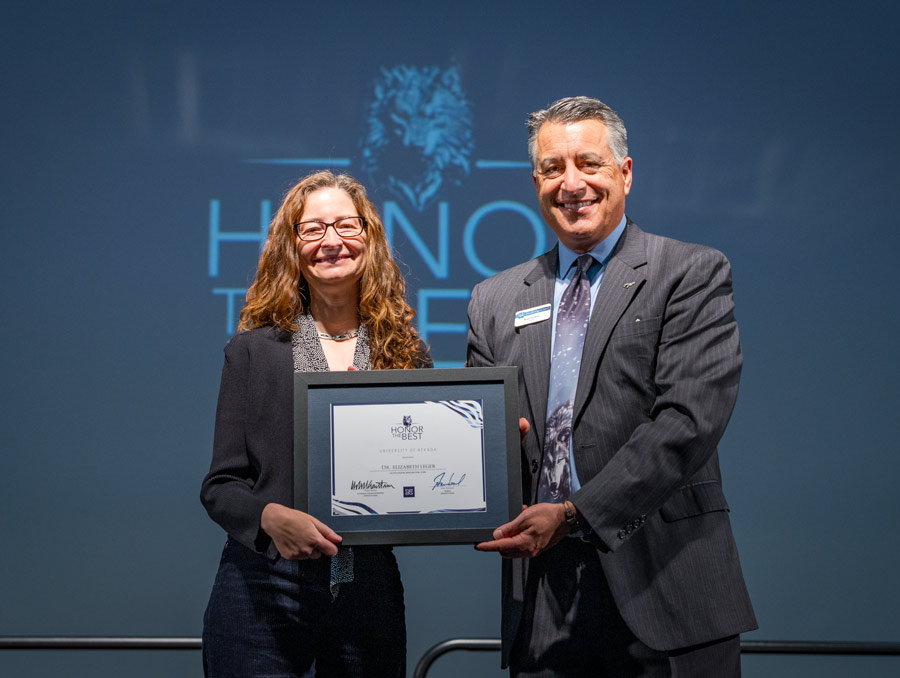Beth Leger and Brian Sandoval smile for a photo, each holding one side of a framed certificate.