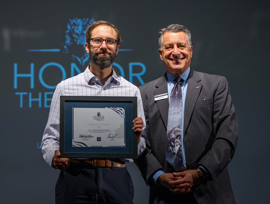Chris Barile and Brian Sandoval smile for a photo, with Barile holding a framed certificate.