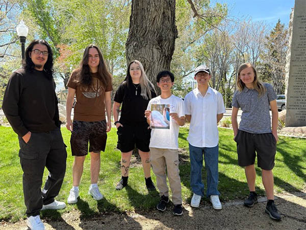 Six people, one holding a picture of a swan, stand outside.