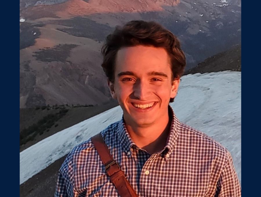 A smiling man posing against a background of snow-capped mountains.