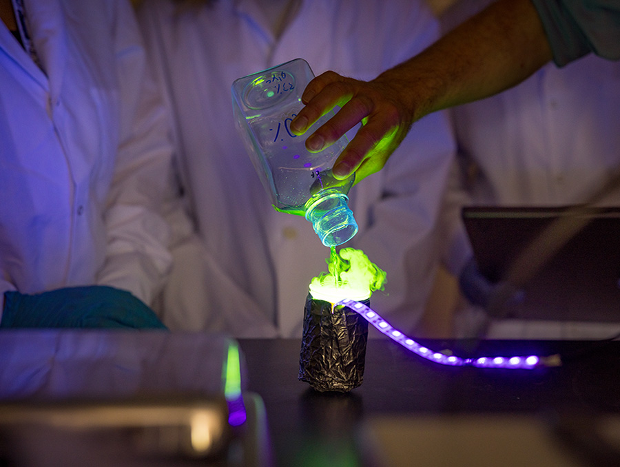 A person's hand pouring a liquid that is glowing in the lab.