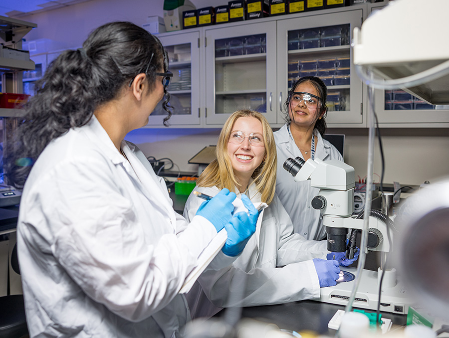 Three students working with a microscope in the lab.