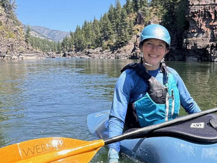 A woman in a blue helmet and vest paddling a blue kayak.