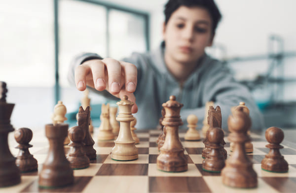 A boy reaches out for a figurines positioned on a checkered dark and light brown board.