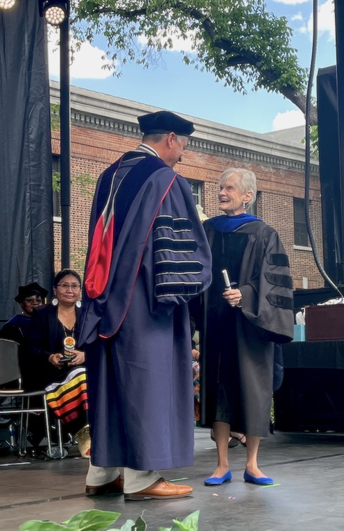 President Sandoval facing Marilyn Newton on stage during the commencement ceremonies as he gives her an honorary degree. They both smile at one another and wear commencement robes.