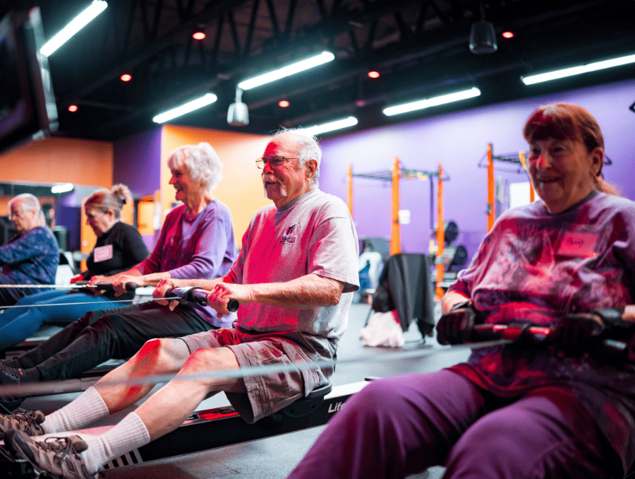 Older adults exercising with rower machines inside a gym during a fitness class